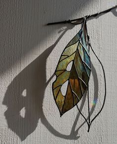 a stained glass leaf hanging on the side of a white wall with sunlight coming through it