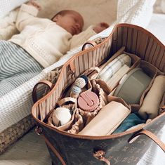 a baby laying in a bed next to a suitcase filled with personal items and toys