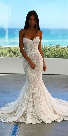 a woman in a white wedding dress posing for a photo with the ocean in the background