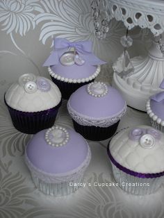 cupcakes decorated with purple and white icing are on a table next to a chandelier