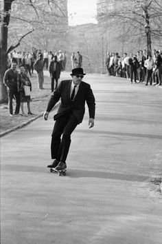 a man riding a skateboard down a street next to a sidewalk filled with people