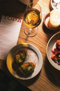 a wooden table topped with two plates of food and glasses of wine next to each other