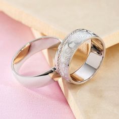 two wedding rings sitting on top of a pink and beige cloth covered table next to each other