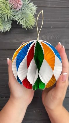 a hand holding a multicolored ornament on top of a wooden table