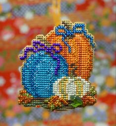 a cross stitch ornament hanging from a string on a colorful wallpapered background