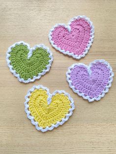 four crocheted hearts sitting on top of a wooden table