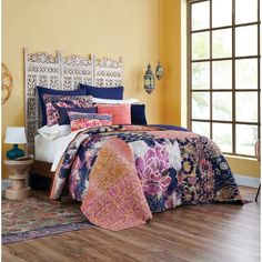 a bed in a room with yellow walls and wooden flooring that has a colorful comforter on it