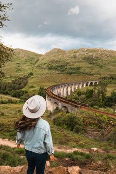 a woman wearing a white hat looking at a train on the tracks in the mountains