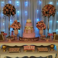 a table topped with a pink and gold cake next to two tall vases filled with flowers