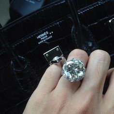 a person's hand holding a diamond ring in front of a black purse with other items