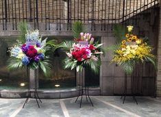 three vases filled with different types of flowers sitting on metal stands in front of a building