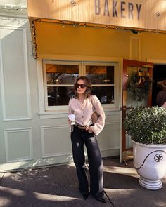 a woman standing in front of a bakery holding a cup