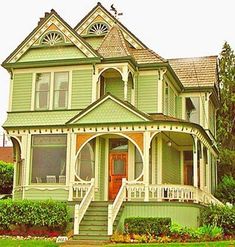 a large green house with white trim on the front porch and two story stairs leading up to it's second floor