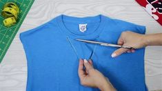 a person cutting fabric with scissors on top of a blue t - shirt and measuring tape