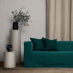 a green couch sitting next to a tall white vase