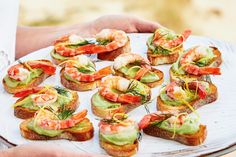 there are many appetizers on the plate in the person's hands, including shrimp and avocado