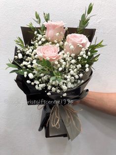 a bouquet of pink roses and white baby's breath is held by a hand