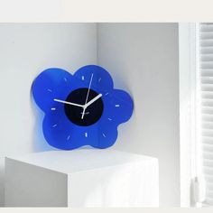 a blue flower shaped clock sitting on top of a white pedestal next to a window