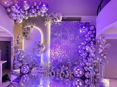 a purple and white wedding setup with balloons on the wall, flowers in vases