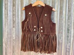 Supercute kid's vintage suede vest.  Original from the 1970's!   This piece is a lovely rich chocolate brown with long fringe and is embellished with silver studs. Size Extra Small. Measurements: Chest: 61 cm / 24 inches Length (Including fringe): 44 cm / 17.25 inches This item is one of a kind. BUYING VINTAGE: While all care is taken to state any obvious faults, please note that when you buy a vintage or preloved item, they may show small signs of ageing, wear and/or repair. Visit my website   https://phoenixmenswear.com.au/ Lots of fun stuff for guys and girls...!! Please note that if you are ordering from anywhere outside of Australia please add your phone number as it is now required for delivery.  Thanks much. Brown Fringe Vest For Festival, Festival Fringe Brown Vest, Brown Fringe Vest For Fall, Bohemian Brown Vest With Fringe, Brown Bohemian Vest With Fringe, Bohemian Brown Fringe Vest, Brown Bohemian Fringe Vest, Brown Sleeveless Fringe Vest, Western Vests