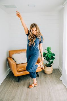 a woman standing in front of a couch pointing to the ceiling with her right hand