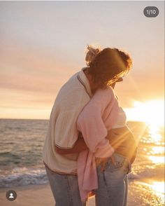 a woman standing on top of a beach next to the ocean holding onto a pink scarf