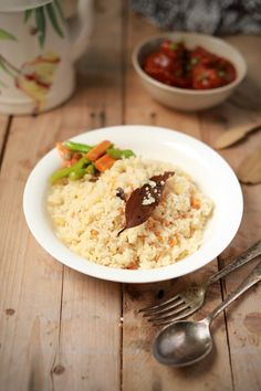 a white bowl filled with rice and veggies next to silverware on a wooden table