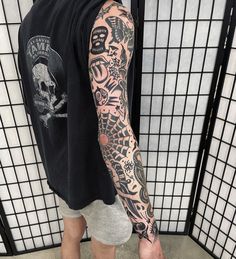 a man with a tattoo on his arm standing in front of a tiled wall and wearing white sneakers