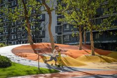 a man riding a skateboard down a street next to trees and grass in front of a tall building