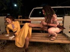 two women sitting on a wooden bench in front of a white van and one woman with dreadlocks