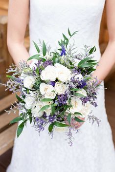 a bridal holding a bouquet of white roses and lavenders in her hands with greenery