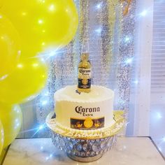 a birthday cake with a bottle of corona beer on top and balloons in the background