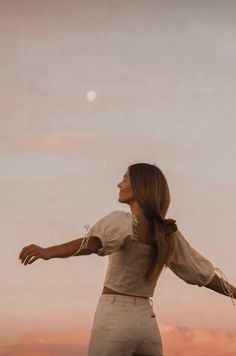 a woman standing on top of a hill with her arms spread out in the air