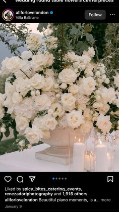 a vase filled with white flowers sitting on top of a table next to two candles