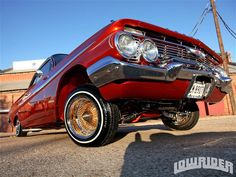 an old red car parked in front of a brick building with gold rims on it's tires