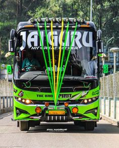 a green and black bus driving down a street next to a fence with trees in the background