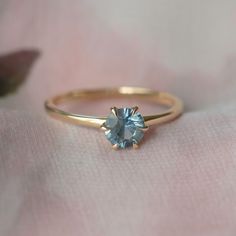 a gold ring with a blue topazte sits on a pink cloth next to a flower