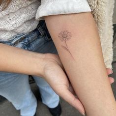 a woman with a small tattoo on her arm holding a dandelion in her hand