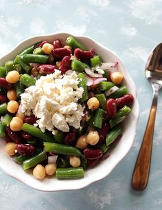 a bowl filled with beans, green beans and feta cheese next to a spoon