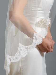 a woman wearing a white wedding veil with lace on the edge and an appliqued belt around her waist