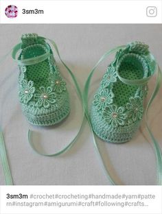 a pair of green crocheted baby shoes on a white surface with a light green ribbon