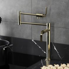 a kitchen sink with gold faucet and marble counter top next to black pots