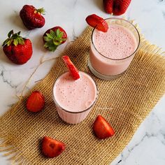 two glasses filled with strawberry smoothie next to strawberries