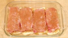 four pieces of meat in a glass dish on a wooden table with sauce and seasoning