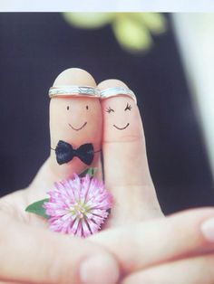 two fingers with faces drawn on them holding a flower