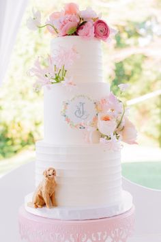 a wedding cake with pink flowers and a teddy bear on the table next to it