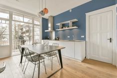 a kitchen with blue walls and wooden flooring next to a dining room table surrounded by chairs