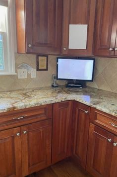 a kitchen with wooden cabinets and marble counter tops, along with a computer monitor on the corner