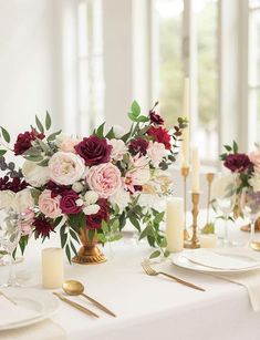 the table is set with white and red flowers, gold place settings, and candles