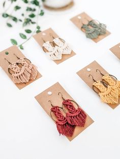 six pairs of earrings with tassels are displayed on the table next to a plant